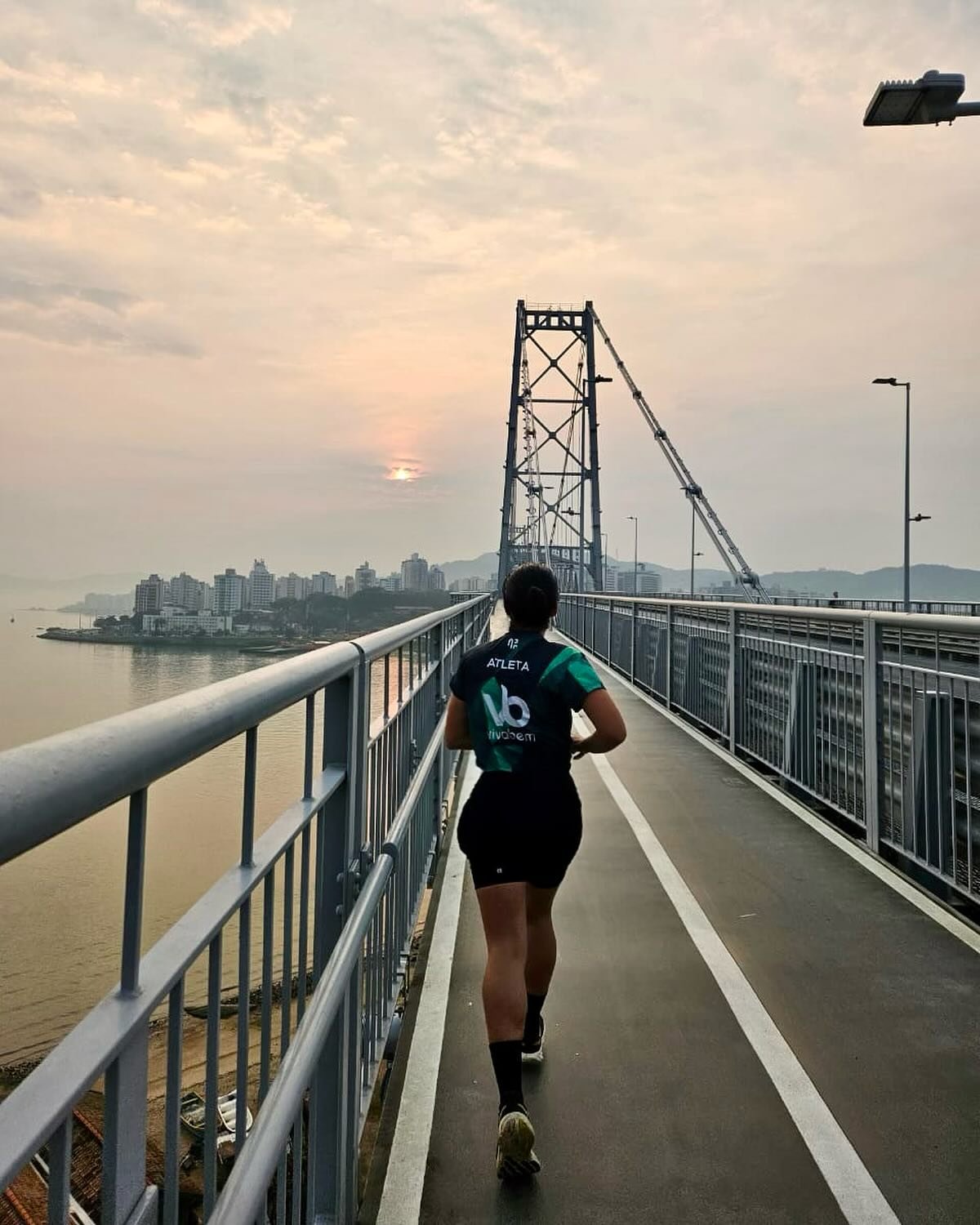 Corredora da Viva Bem atravessando a ponte Hercílio Luz ao pôr do sol em Florianópolis